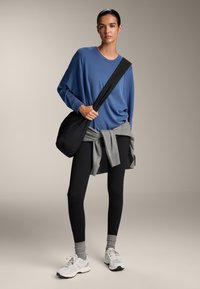 Modra dolga majica, siva ohlapna obleka okoli pasu, črne legice, sive ankle nogavice in bele tenisice. Črna torba je premetana čez ramo.