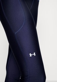 Mörkblå sport leggings med en slät textur, med en vit logotyp på underbenet och kontrasterande sömdetaljer.