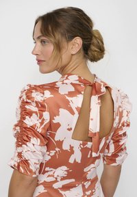 Blumenkleid aus Satin in Rost mit weißen Mustern, mit Puffärmeln und einem Schlüsselloch-Rücken mit einer Schleifendetail. Glatte Textur.