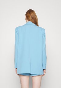 Blazer over-size azzurro chiaro realizzato in tessuto liscio, con collo a rever, maniche lunghe e un'ventilazione posteriore singola.