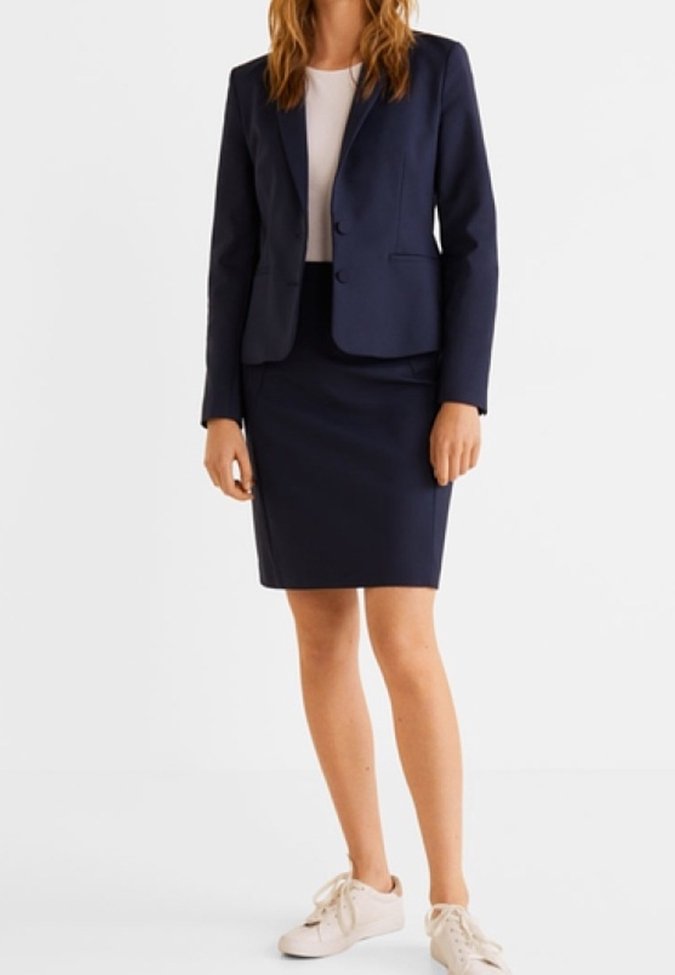 Námořnický modrý blazer se dvěma knoflíky, nošený přes bílý top, spárovaný s odpovídající námořnickou sukní a bílými teniskami. Hladká textura, přiléhavý střih.