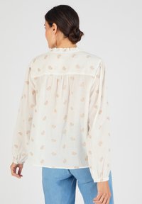 Blusa chiara con maniche lunghe, scollatura arricciata e sottili motivi di foglie beige; realizzata in un tessuto morbido e leggero.