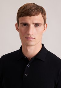 Schwarzes Poloshirt mit Kragen und zwei Knöpfen auf der Vorderseite. Der Stoff wirkt glatt und gestrickt und hat eine enge Passform.