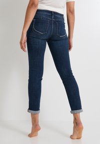 Jeans de mezclilla azul oscuro con una silueta ajustada, puños enrollados y bolsillos traseros. La tela tiene una textura suave y un ligero estiramiento.