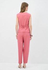 Haut sans manches rose avec un détail en nœud à l'arrière, associé à un pantalon rose ample. Texture de tissu lisse, design minimaliste.