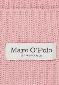 Gebreide roze stof met een geribbelde textuur en een wit stoffen label met daarop in het zwart "Marc O'Polo EST. IN STOCKHOLM".