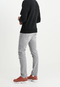 Jeans gris clair avec une coupe slim et des poches arrière discrètes, associés à des baskets rouges et un sweatshirt noir. Fabriqués en matériau denim.