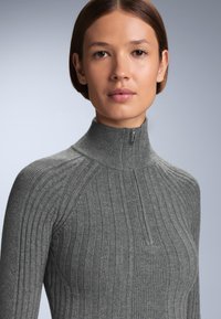 Grå ribbad polotröja med halvdragkedja och figurnära design. Tyget har en mjuk, strukturerad yta och slät finish.