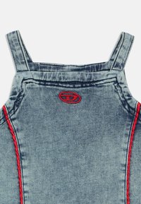 Traper hlače na tregere u svijetlo plavoj boji s crvenim šavovima. Ima podesive naramenice, okrugli logotip na zakrpi i teksturiranu tkaninu.