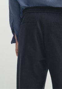 Donkerblauwe joggingbroek met elastische tailleband, voorzien van twee achterzakken en een zachte textuur. Het shirt is lichtblauw met een relaxed fit en knoopdetails.