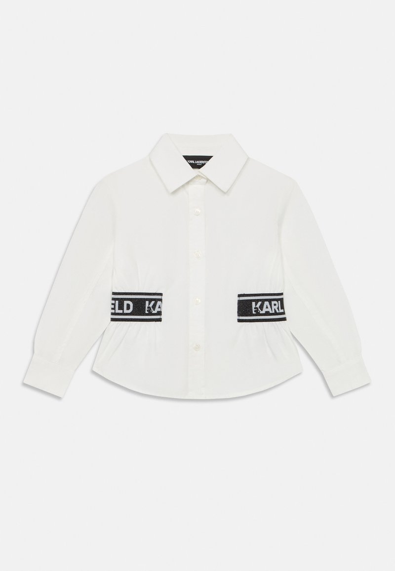 Camisa branca de mangas longas com gola clássica, apresentando bandas elásticas pretas na cintura com a marca "KARL". Textura de tecido suave.