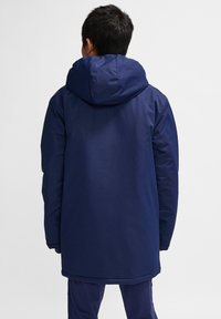 Marineblauwe parka met capuchon, gemaakt van een gladde, waterafstotende stof. Kenmerkt zich door een lange snit en elastische manchetten. Achteraanzicht weergegeven.