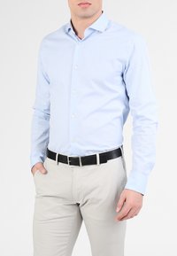 Camicia azzurro chiaro con taglio slim, maniche lunghe e texture liscia. Abbinata a pantaloni beige e una cintura nera.
