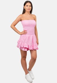 Roze strapless jurk met een smocked bodice en een gerimpelde zoom. Gemaakt van structuurstof. G gedragen met witte sneakers.