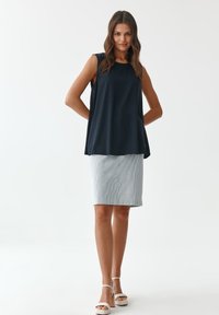 Námornícky bezrukávový top skombinovaný s prúžkovanou svetlomodrou pántovou sukňou. Biely sandále na podpätku dopĺňajú outfit. Hladké tkaniny, uvoľnený strih.