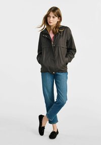 Czarna, lekką kurtka z zamkiem z przodu, zatrzaskami i dwiema bocznymi kieszeniami, w połączeniu z jasnoniebieskimi dżinsami i czarnymi butami.