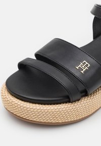 Czarna skórzana sandał z dwoma szerokimi paskami, okrągłym noskiem oraz plecioną podeszwą na platformie z złotym akcentem logo.