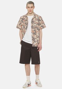 Kortermet skjorte med et flerfarget abstrakt mønster, beige bakgrunn, kombinert med mørkebrune shorts og hvite sneakers.