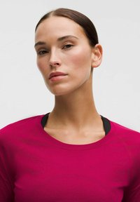 Fitted, langwerpige top van felle roze stof, met een ronde hals en een gladde textuur, gelaagd over een zwarte sporttop.