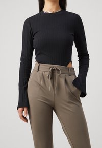 Black ribbed long-sleeve top with a rounded neckline and cut-out sides, paired with beige high-waisted trousers featuring a drawstring waist.