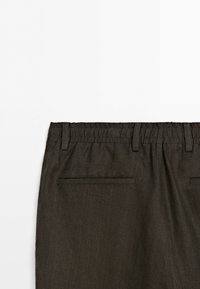 Dark brown pants waistband with elastic back and two horizontal welt pockets without buttons or zippers.