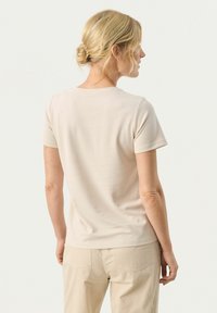 T-shirt beige aderente con maniche corte e colletto tondo classico. Tessuto liscio con design semplice, indossato con pantaloni chiari.