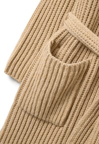 Beige gebreide cardigan met brede ribbelstructuur, voorzien van een open voorkant, lange mouwen en een grote zak aan de linkerkant.