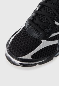 Black athletic shoe with a textured mesh upper and silver synthetic accents, featuring black laces and a cushioned sole.