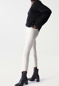 Beige jeans with embroidered patterns on the side, paired with a black v-neck sweater and black ankle boots with a chunky heel.