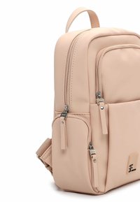 Plecak w kolorze brzoskwiniowym o gładkiej, matowej powierzchni. Posiada dwie komory zamykane na suwak oraz boczną kieszeń z akcentami w postaci srebrnych elementów metalowych.