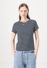 Camiseta a rayas en azul marino y blanco con mangas cortas y cuello redondo. Tejido suave y acanalado con un pequeño logo cerca del cuello.