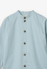 Camicia azzurra chiara con bottoni e tessuto testurizzato, dotata di colletto rotondo. Presenta bottoni scuri lungo la parte anteriore per la chiusura.