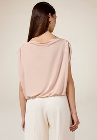 Blusa in morbido tessuto rosa chiaro con vestibilità comoda, scollatura drappeggiata e maniche corte arricciate, abbinata a pantaloni ampi color crema.