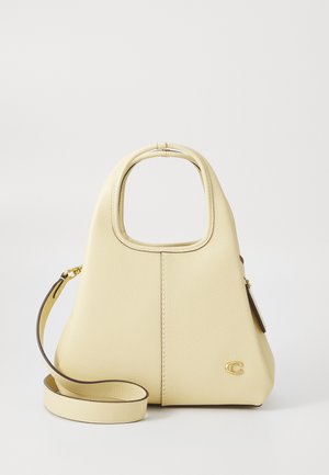 Kremowa skórzana torebka z zaokrąglonym górnym uchwytem, odpinanym paskiem na ramię oraz małym złotym logo na przednim, dolnym prawym rogu.