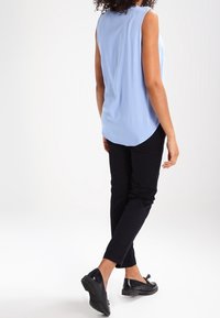 Ljusblå ärmlös topp med rundad nederkant, tillsammans med svarta slim-fit byxor och svarta skor med dekorativa detaljer.