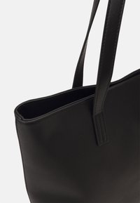 Mustat nahka-olkalaukku, jossa on kaksi litteää kahvaa, avoin yläosa ja sileä pinta. Huomaamattomat ompeluyksityiskohdat reunoissa.