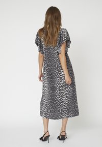 Rochie maxi în imprimeu leopard gri și alb. Material moale, mâneci fluente, siluetă fluidă, care ajunge până la jumătatea gambei. Pantofi cu toc înalt negri.
