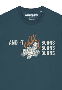 Teal katoenen t-shirt met een grafisch ontwerp van stammen en vlammen, met de tekst "EN HET BRANDT, BRANDT, BRANDT" in witte en oranje letters.
