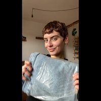 Μπλε πετσέτα διπλωμένη και τυλιγμένη σε διαφανές πλαστικό, με λεία υφή. Άτομο που την κρατά μπροστά από έναν μινιμαλιστικό εσωτερικό χώρο.