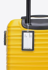 Žlutý tvrdý kufr s vroubkovaným povrchem, teleskopickou rukojetí, připojenou štítkem na zavazadlo a zámkovým mechanismem na boku.