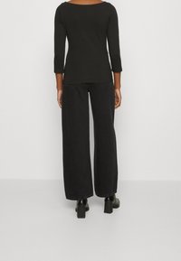 Svart långärmad topp med bred rundringning, tillsammans med löst sittande svarta jeans. Båda plagg har en enhetlig färg och minimalistiska detaljer.