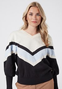 Knitted pullover sweater featuring a V-neck, black base, and chevron pattern in cream, light blue, and black. Knit texture with ribbed cuffs.