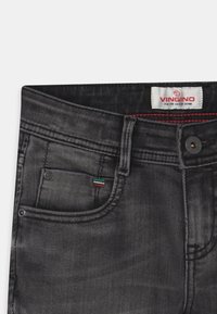 Černé džíny z denimu s jemně vybledlým vzhledem, designem pěti kapes a malým červeným, zeleným a bílým akcentem v blízkosti přední kapsy.