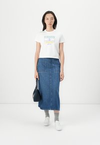 T-shirt blanc cropped avec un logo multicolore, associé à une jupe midi en denim taille haute. Des chaussettes gris clair et des baskets blanches complètent le look.