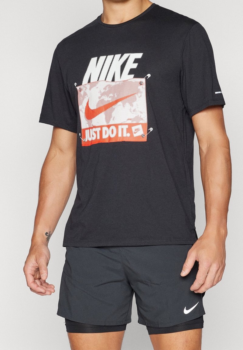 Černé tričko s krátkým rukávem vyrobené z bavlny, s bílým logem "NIKE" a červenou grafikou "JUST DO IT.", s dvěma očky v rozích.