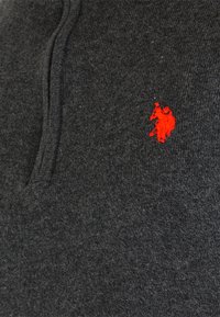 Mørkegrå uldpullover med en tekstureret finish, der har et lille rødt broderet logo på brystet og en krave-design med placket.