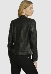 Black leather jacket featuring a fitted design, seam detailing, and a slightly flared hem. Paired with black pants and accentuated pockets.
