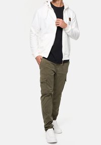 Hvid hættetrøje med lynlås og hætte, kombineret med olivengrønne cargobukser med sidelommer og hvide sneakers.