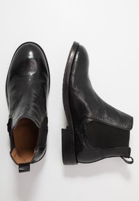 Černé kožené kotníkové boty s hladkým povrchem, elastickými bočními panely a pevným podpatkem, vybavené poutkem na zadní straně pro snadné obutí.