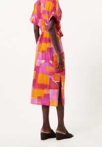 Vestito midi colorato con un motivo di forme rosa, arancioni e gialle; maniche corte, vita elastica e spacco laterale. Indossato con tacchi marroni.